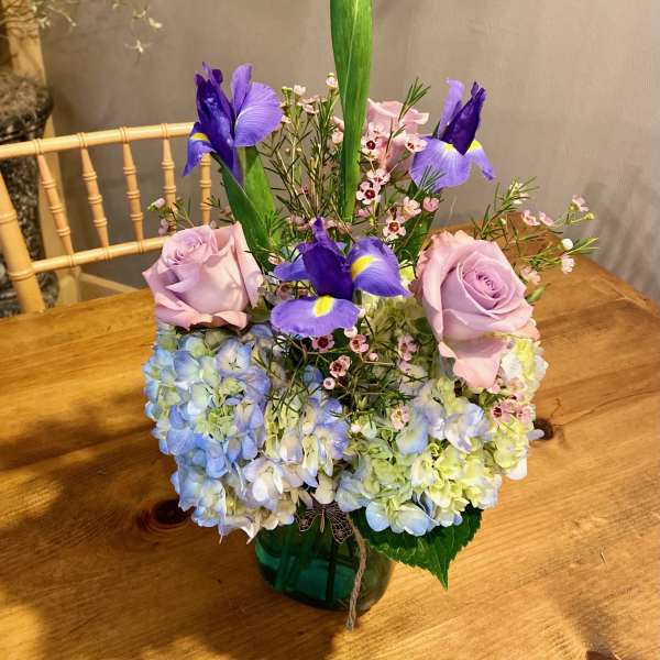 Bouquet of lavender roses, blue hydrangeas, and purple irises in a vase