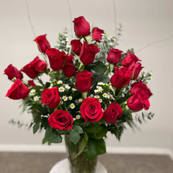 Red roses arranged in a clear glass vase with small white filler flowers
