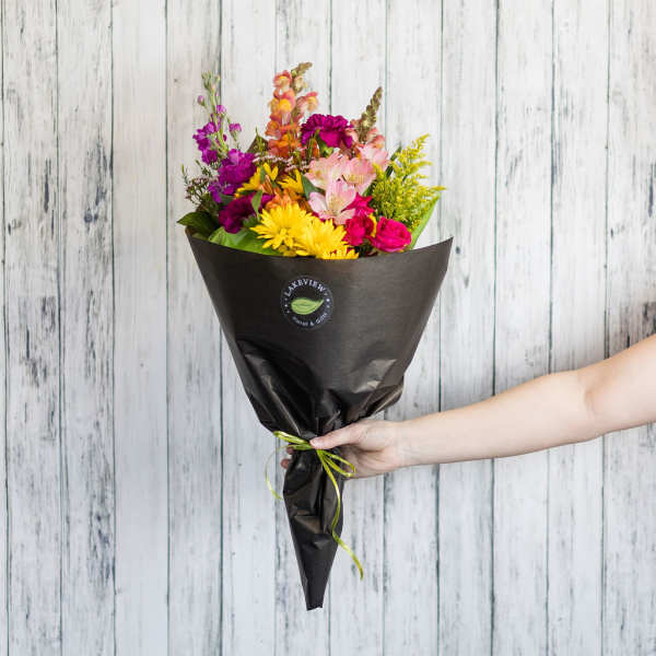 Handheld bouquet of mixed bright flowers wrapped in black paper