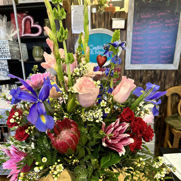 Mixed bouquet of pink, red, and blue flowers in a glass vase