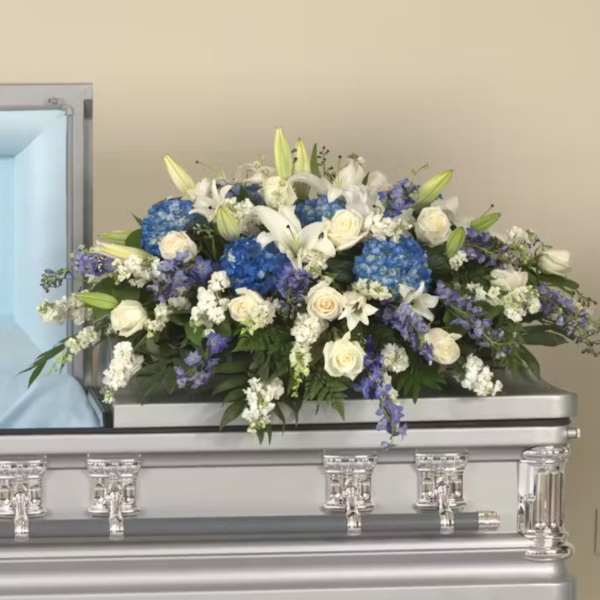 Large white and blue casket spray with roses, lilies, and hydrangeas on a silver casket.