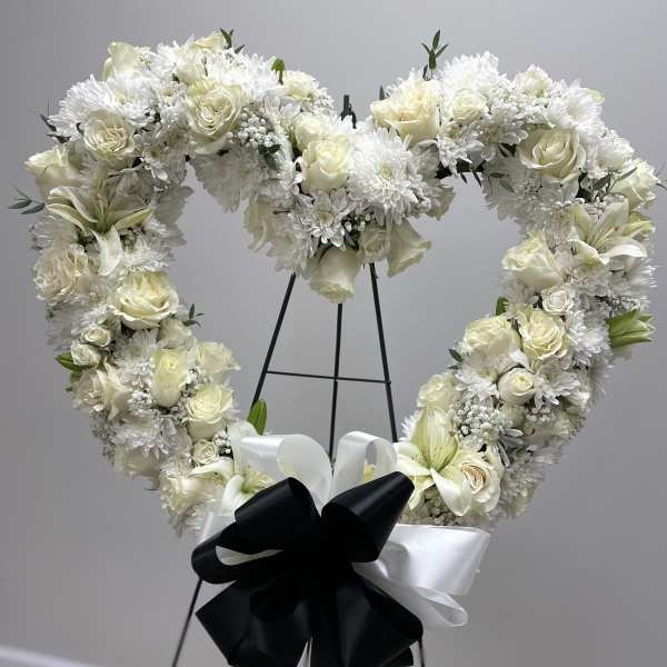 Heart-shaped white floral wreath on an easel with black and white ribbon