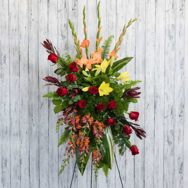 Tall floral arrangement with red roses, yellow lilies, and orange blooms