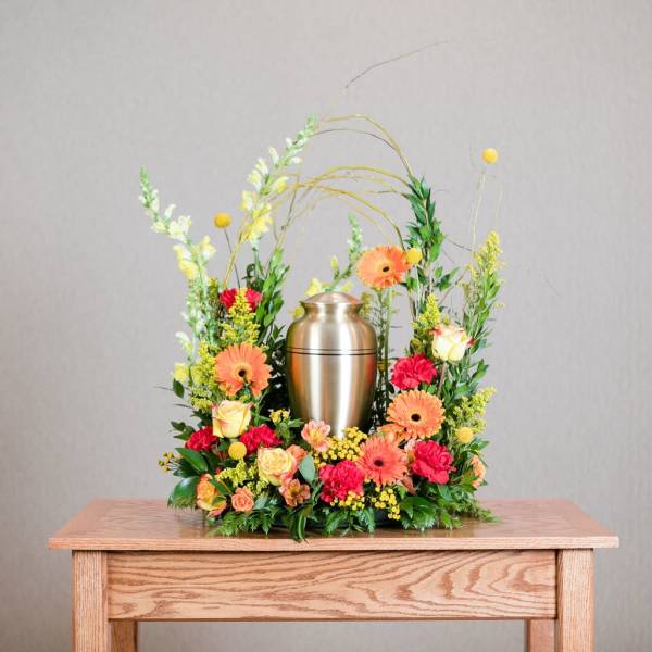 Floral urn arrangement with orange gerberas, roses, and a silver urn