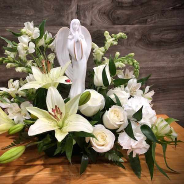 White lilies and roses arranged around a white angel figurine
