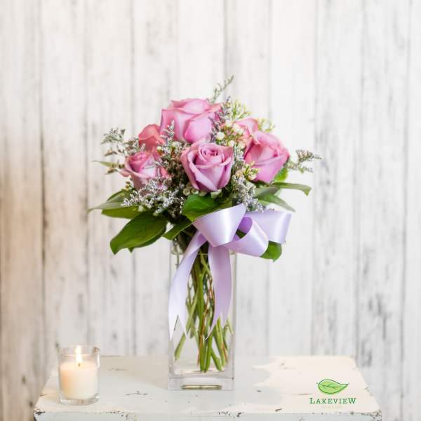 Pink roses in a clear glass vase with a lavender ribbon and candle