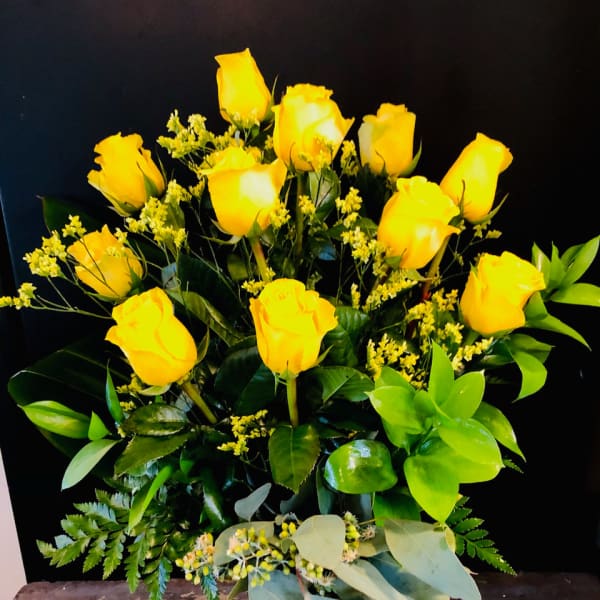Yellow roses arranged in a clear glass vase with mixed greenery