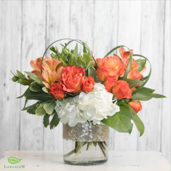 Orange roses and white hydrangeas in a glass vase with greenery