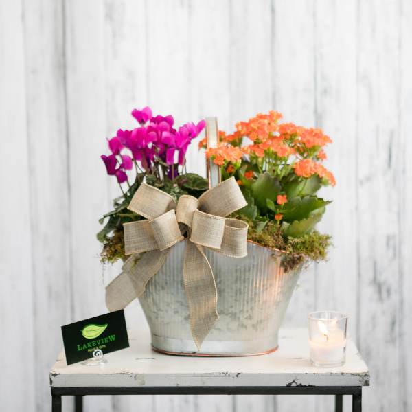 Pink and orange flowering plants in a metal bucket with a burlap bow.