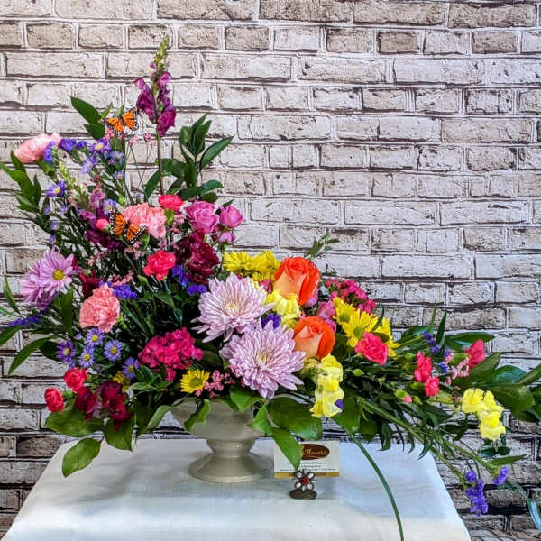 Colorful mixed flower arrangement in a pedestal vase with butterfly accents