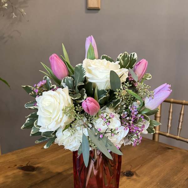Pink tulips and white roses arranged in a red glass vase
