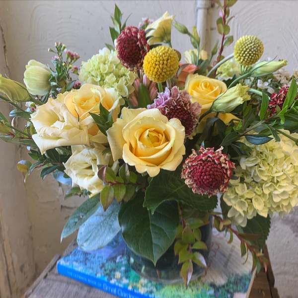 Yellow roses and pale hydrangeas in a glass vase with round accent blooms