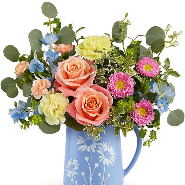 Mixed bouquet of peach roses, yellow carnations and blue blooms in a blue daisy-print pitcher