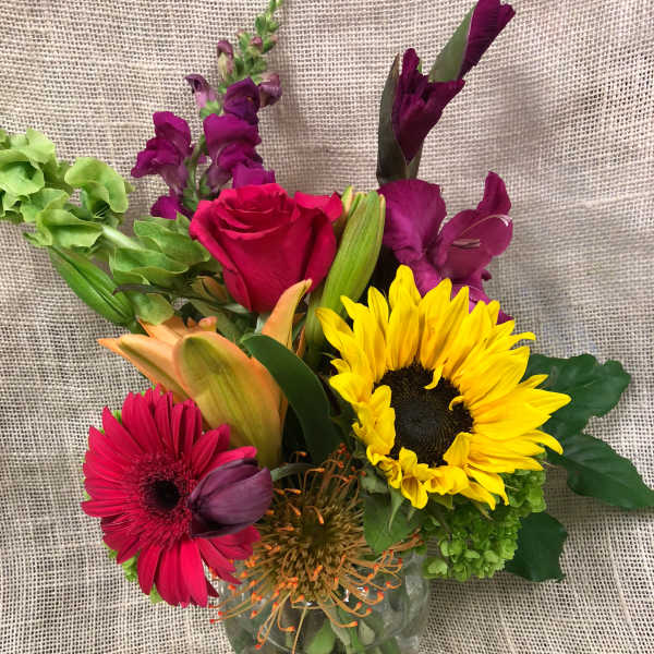 Mixed bouquet in a clear glass vase with a sunflower, rose, and gerbera daisies