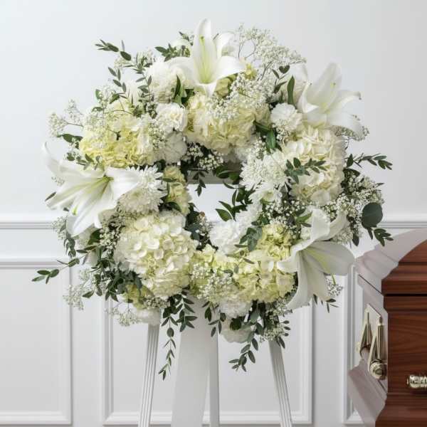 White floral funeral wreath on a stand with lilies and hydrangeas