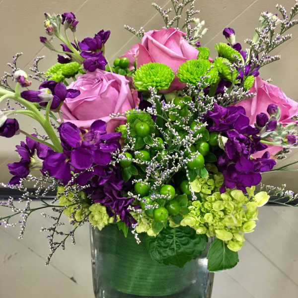 Pink roses and purple flowers arranged in a square glass vase