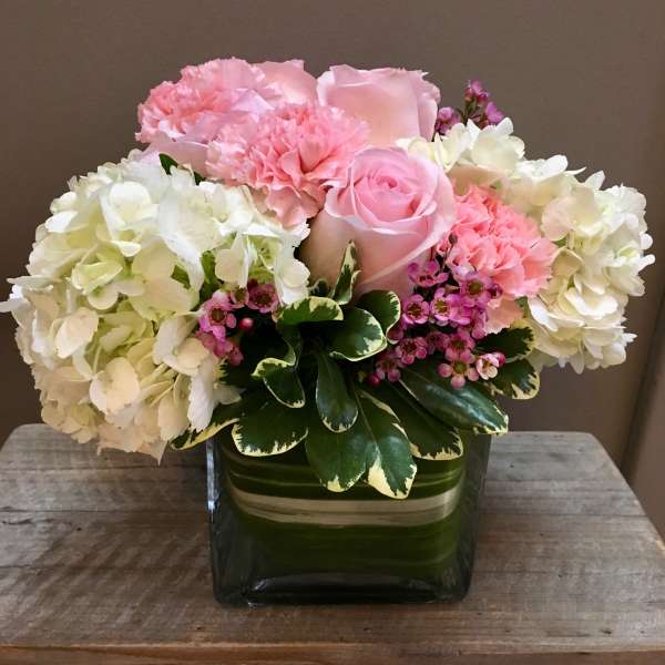 Pink roses and carnations arranged with white hydrangeas in a green glass vase.