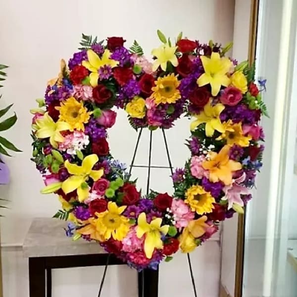 Heart-shaped floral wreath on a stand with yellow lilies and red roses