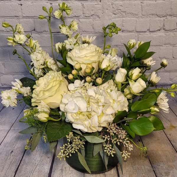 White roses and hydrangeas in a low green vase with mixed greenery