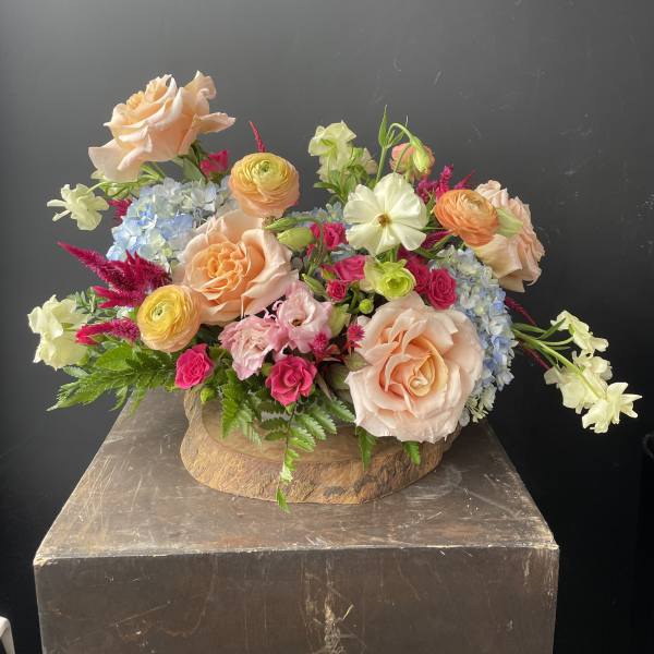 Mixed bouquet of peach roses, pink blooms, and blue flowers in a wooden container