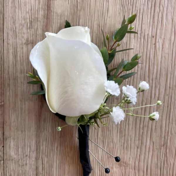 White rose boutonniere with small white filler flowers and greenery