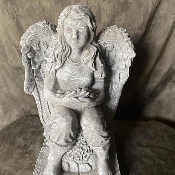 Gray stone angel statue seated with wings and a small bowl in her lap