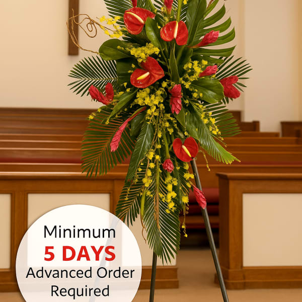 Tall tropical standing spray with red blooms and yellow accents on an easel in a church.