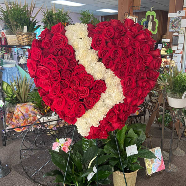 Tall heart-shaped standing spray of red roses with a white floral stripe above two potted green plants
