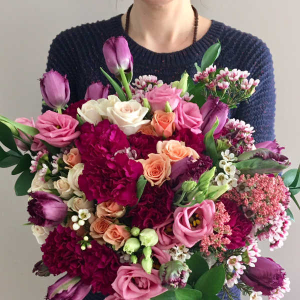 Large bouquet of pink, purple, and peach flowers held by a person