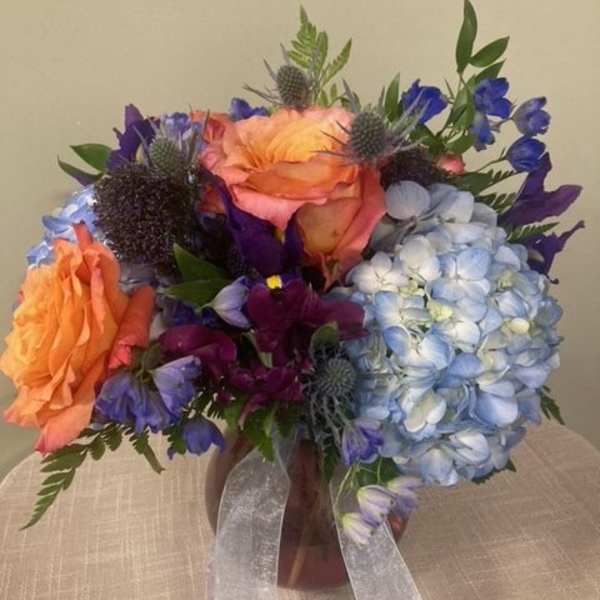 Bouquet of orange, blue, and purple flowers in a vase with ribbon