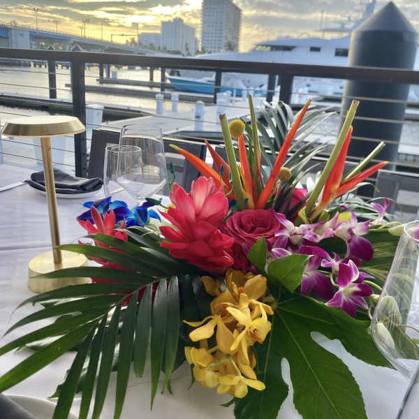 Tropical floral centerpiece with orchids, roses, and bright red blooms