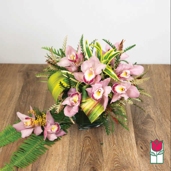 Pink orchid arrangement in a glass vase with tropical leaves