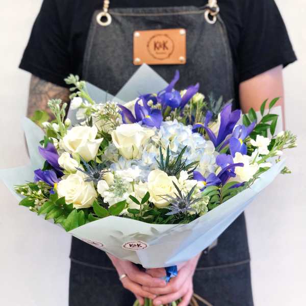 Handheld bouquet of white roses, blue hydrangea, and purple irises