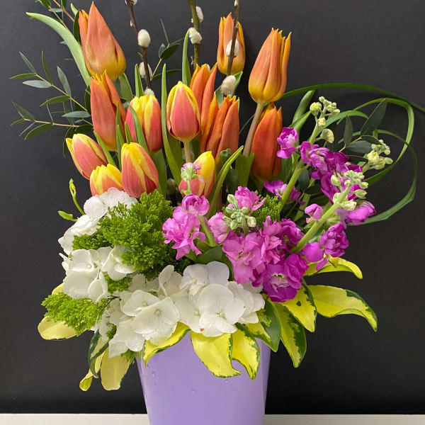 Bouquet of orange tulips, white hydrangeas, and purple flowers in a lavender vase