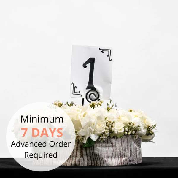 Low white floral centerpiece in a round container with a table number one sign.