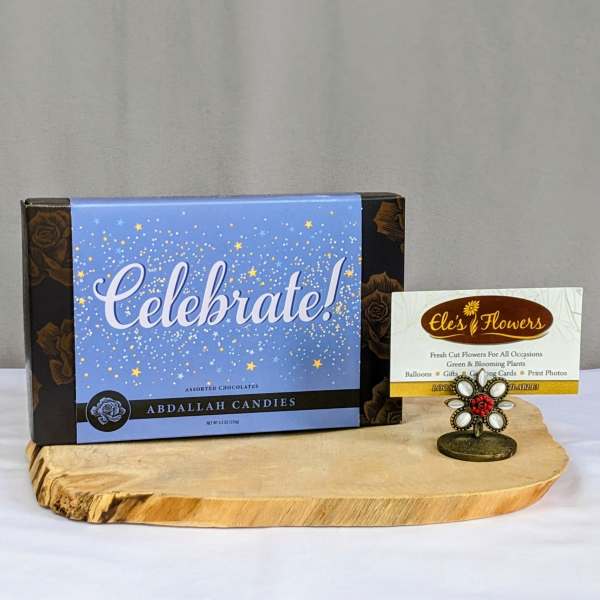 Box of Celebrate assorted chocolates with florist business card on a wood tray