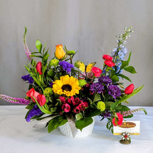 Colorful mixed flower arrangement in a white basket with a butterfly pick