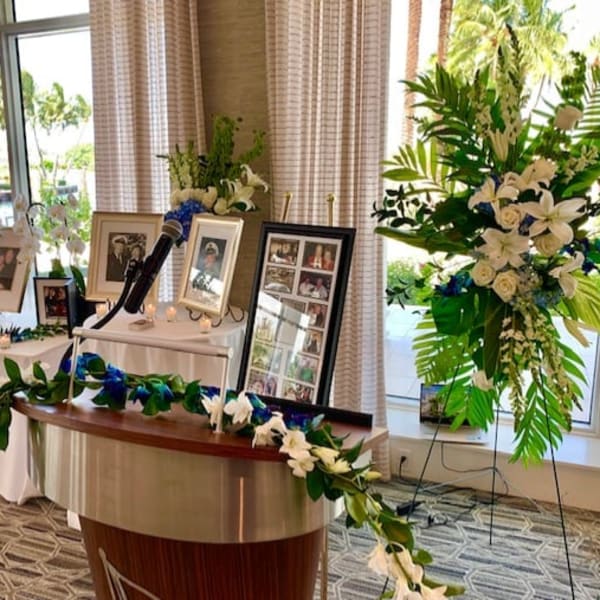 White floral funeral display with framed photos and a microphone stand
