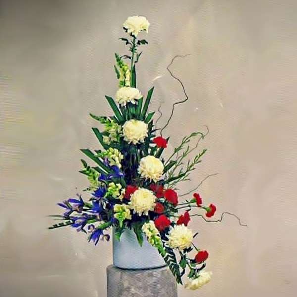 Tall asymmetrical arrangement of white chrysanthemums, red carnations and blue iris in a white vase