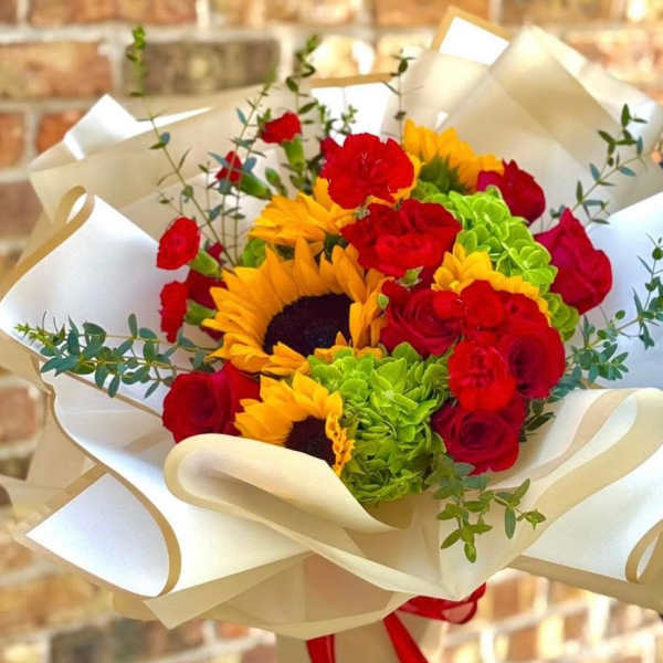 Bouquet of red roses, sunflowers, and green hydrangeas wrapped in cream paper