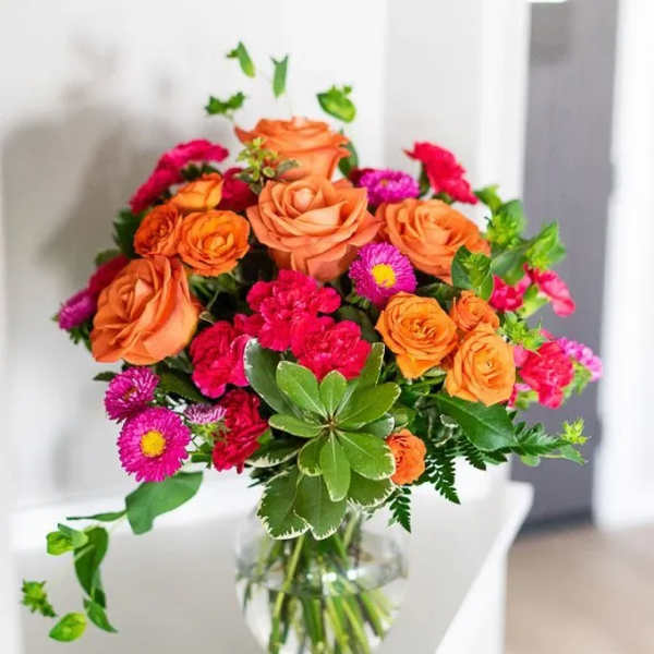 Orange roses and pink flowers arranged in a clear glass vase