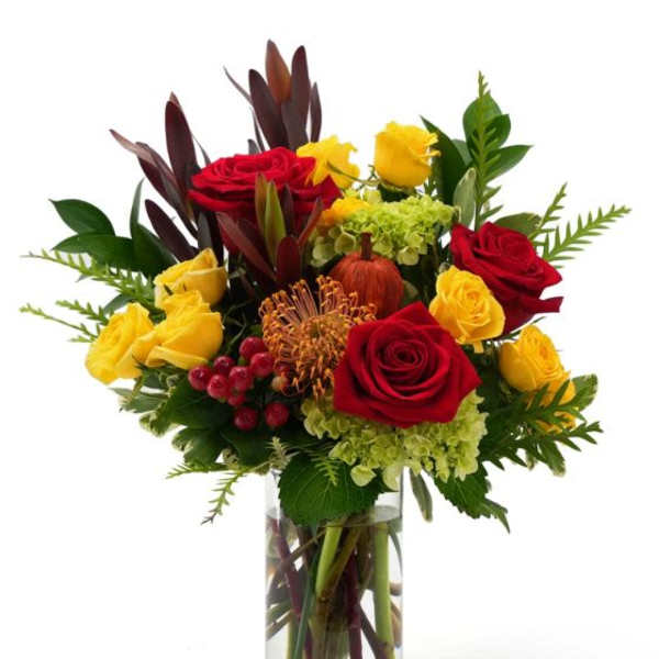 Tall arrangement of red and yellow roses with green hydrangea in a clear glass vase