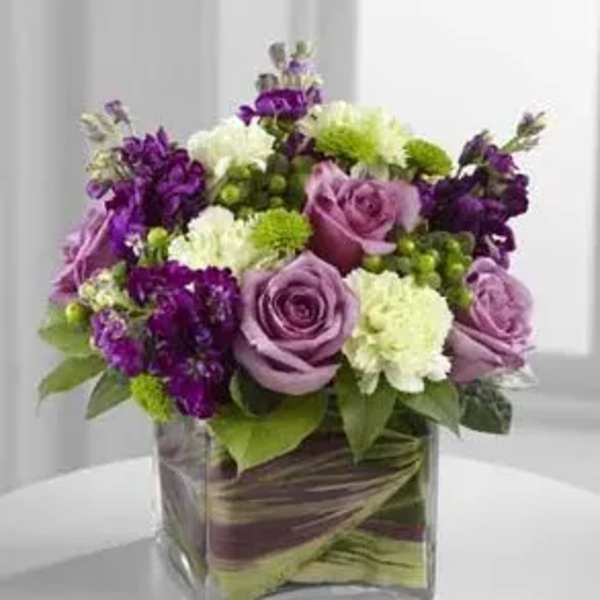 Purple and white floral arrangement in a square glass vase