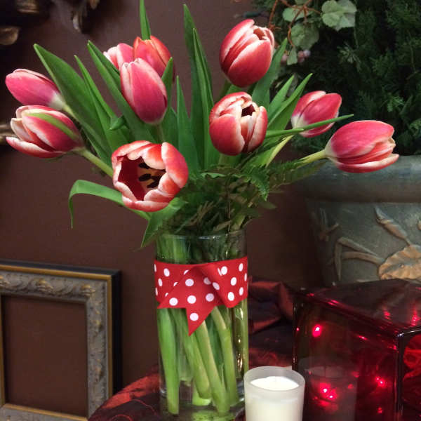 Red and white tulips in a clear vase with polka dot ribbon, next to a small white votive candle.