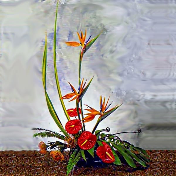 Tall tropical arrangement with orange bird-of-paradise and red blooms in a low container with large leaves.