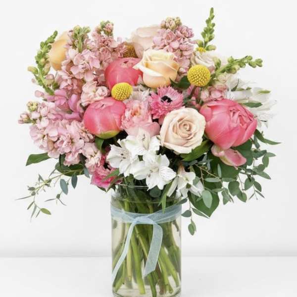Pink and cream flowers arranged in a glass vase with a blue ribbon.