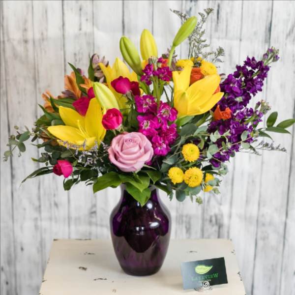 Mixed bouquet of lilies, roses, and purple flowers in a dark vase