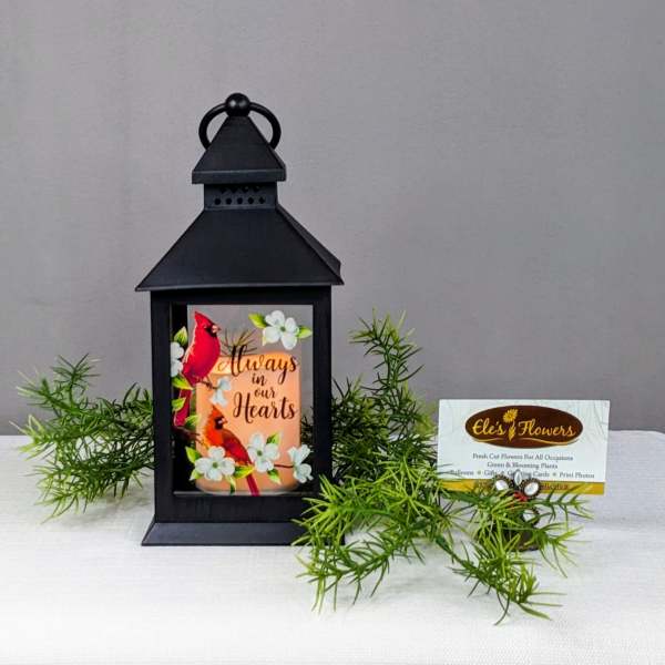 Black lantern with a memorial card and greenery on a white cloth