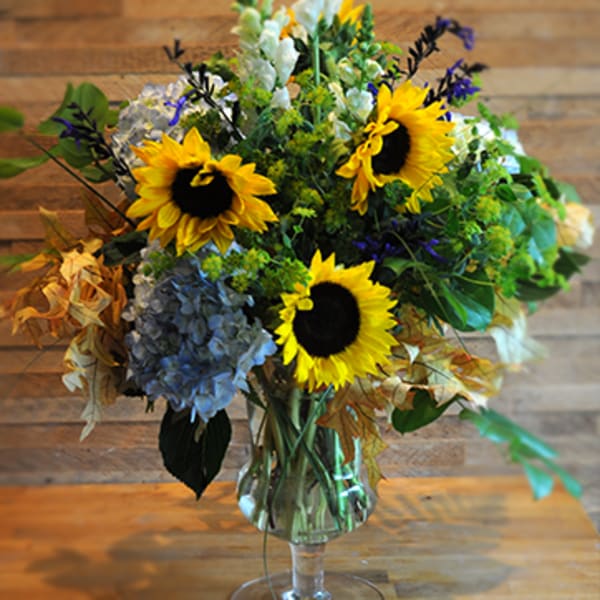 Sunflower bouquet with blue hydrangeas in a clear glass vase