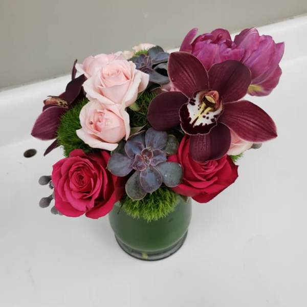 Bouquet of pink roses and dark orchids in a green vase